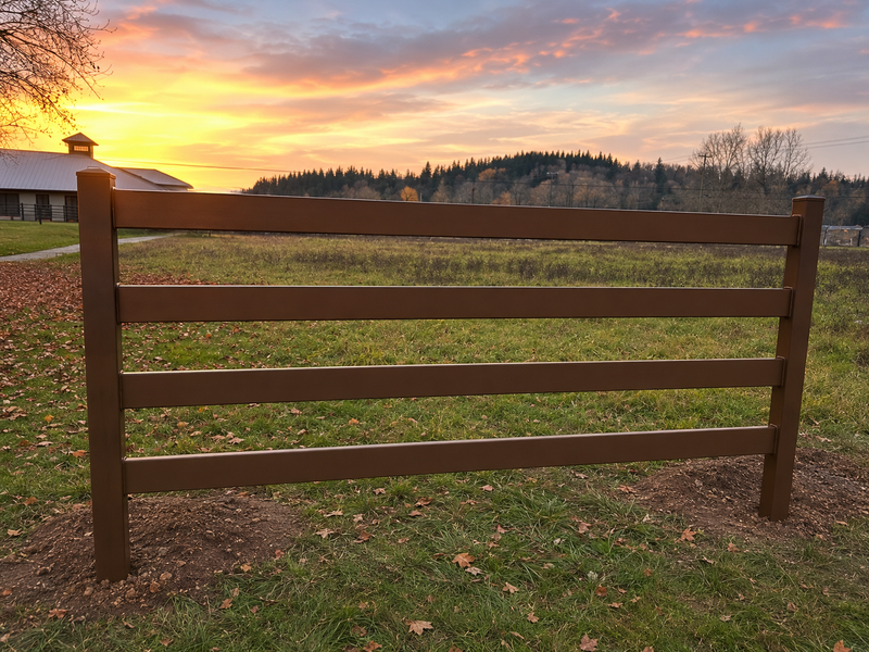 Load image into Gallery viewer, Coffee brown ranch-style horse fence with horizontal rails installed in a rural grassy field, with farm buildings, autumn leaves, and wooded hills in the background.